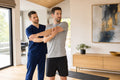 Physical therapist guiding an adult client through a movement assessment in a bright modern residence